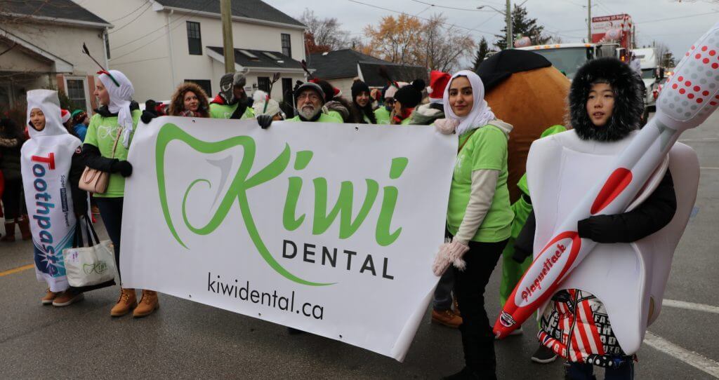 Kiwi Dental team holding a banner at the 70th annual Santa Claus parade in downtown Oakville